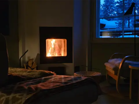 Armchair with a wool blanket in front of the lit stone fireplace