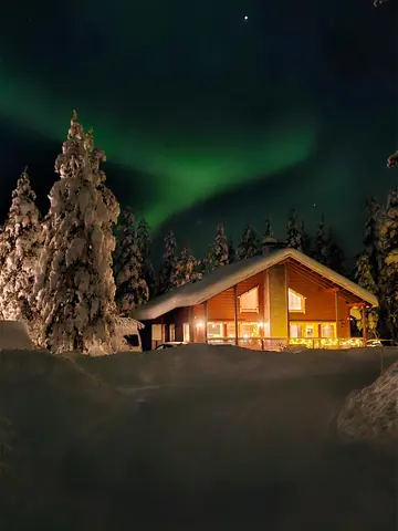 Green northern lights over the lit windows of Chalet Nulkka on a winter night